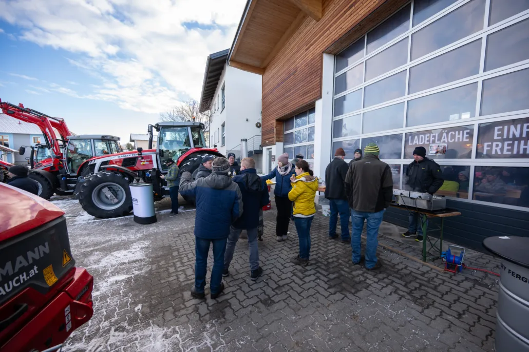 Menschen vor einem Rolltor der Firma Flixeder Landtechnik mit Massey Ferguson Traktoren im Hintergrund