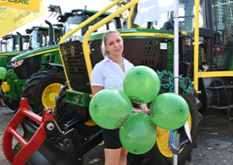 Titelbild: Dame mit 4 grünen Luftballons vor John Deere Traktoren