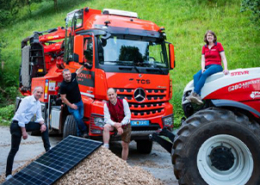 Titelbild mit Mercedes Benz Holzschredder-LKW 3 Männer, PV-Paneel auf Hackschnitzel-Haufen & Frau auf Steyr 6280 Absolut