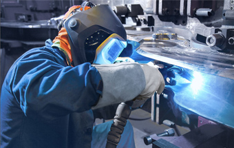 Titelbild: Mensch mit Schutzmaske und Schutzanzug beim Schweißen