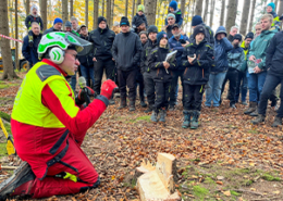 ein Forstarbeiter kniet mit einem Mikro im Wal, rund um ihn steht eine Menschenmenge