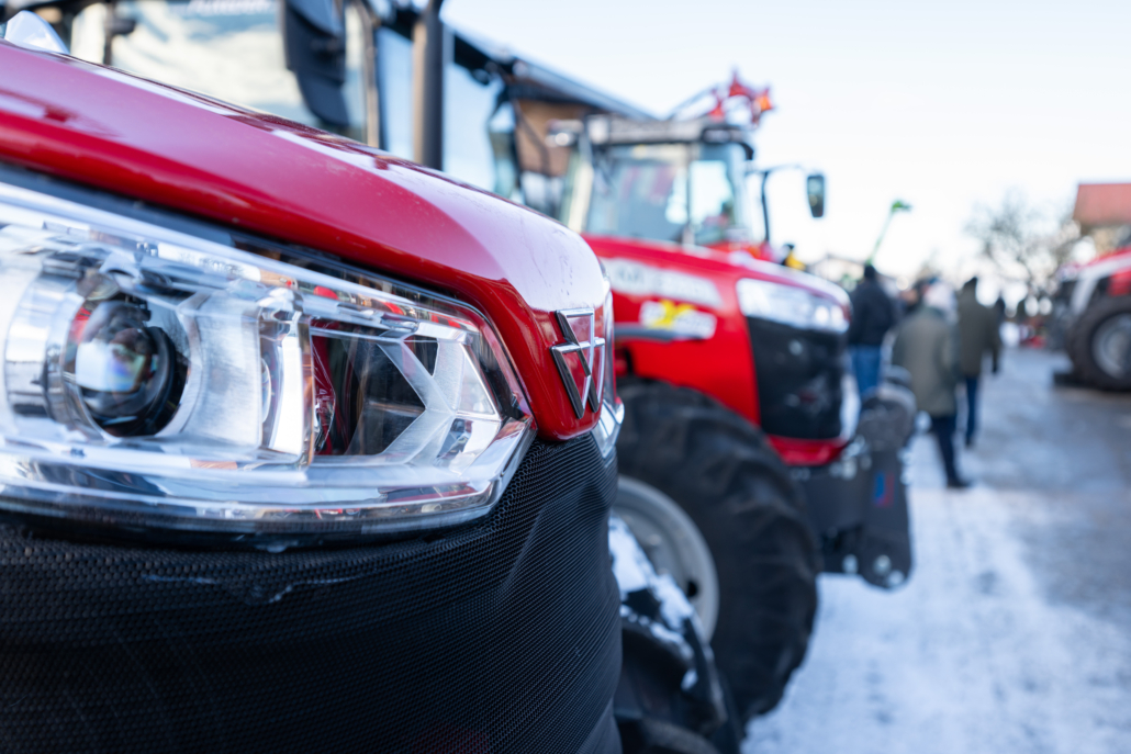 Detailaufnahme Massey Ferguson Motorhaube mit weiteren Massey Ferguson Traktoren und Menschen unscharf im Hintergrund