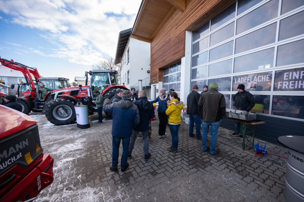 Menschen vor einem Rolltor der Firma Flixeder Landtechnik mit Massey Ferguson Traktoren im Hintergrund